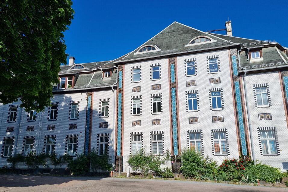 Fassade eines historischen Gebäudes mit Fenstern und bunten Verzierungen, umgeben von Grünanlagen und blauem Himmel.